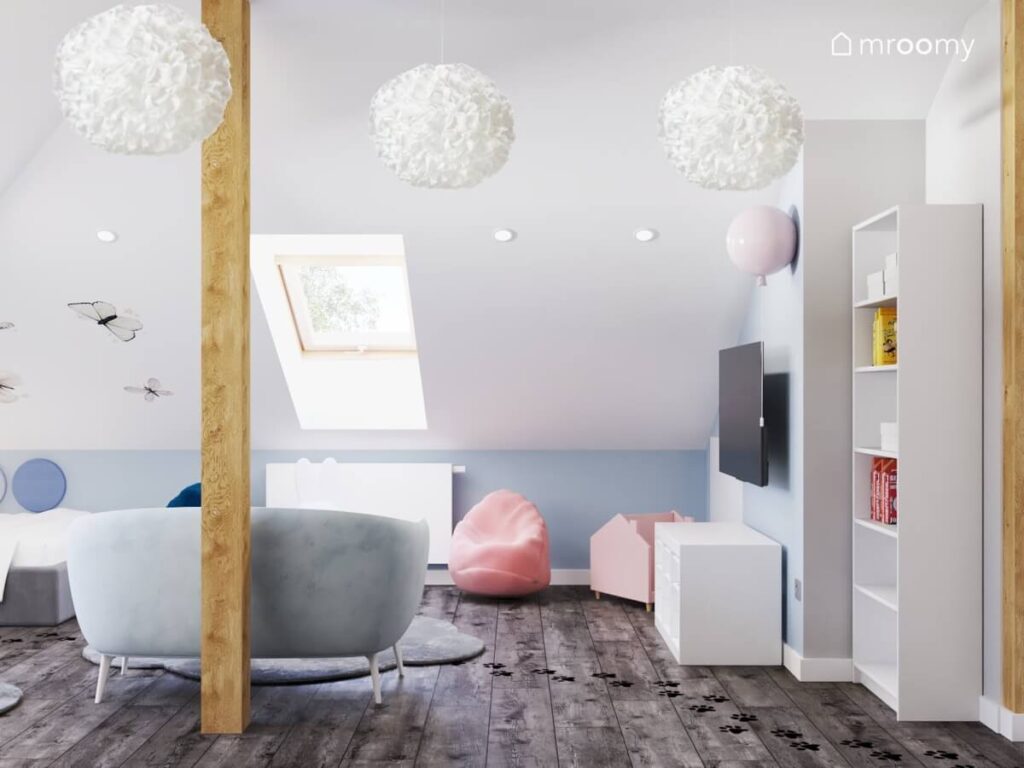 Strefa dzienna w biało błękitnym poddaszowym pokoju dla dziewczynki a w niej błękitna sofa worki do siedzenia różowa biblioteczka oraz ozdobne białe lampy sufitowe