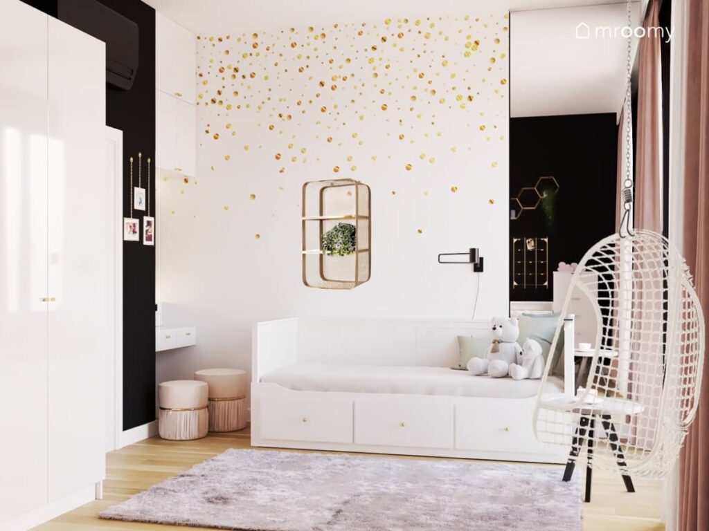 Strefa spania w pokoju dla nastolatki a w niej białe łóżko z szufladami ze złotymi gałkami kremowe pufy a na ścianie biała tapeta w złote kropki lustro oraz mosiężna półka