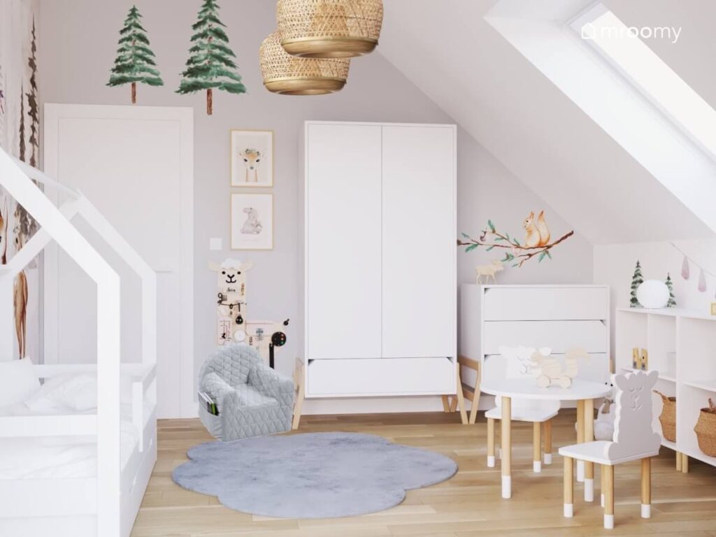 Biała szafa i komoda na drewnianych nogach tablica manipulacyjna w kształcie alpaki szary fotelik oraz ściana uzupełniona leśnymi naklejkami w pokoju dla małej dziewczynki