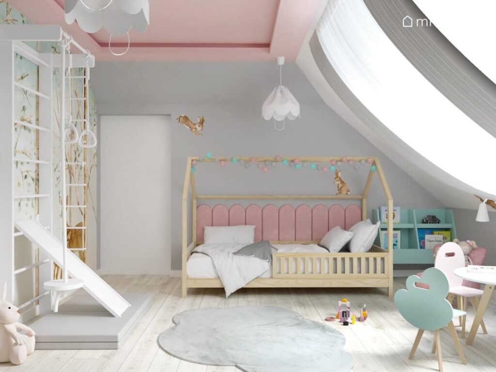 Drewniane łóżko domek uzupełnione girlandą cotton balls oraz różowy panelami ściennymi a także drabinka gimnastyczna i dywanik w kształcie chmurki w pokoju dla dziewczynki