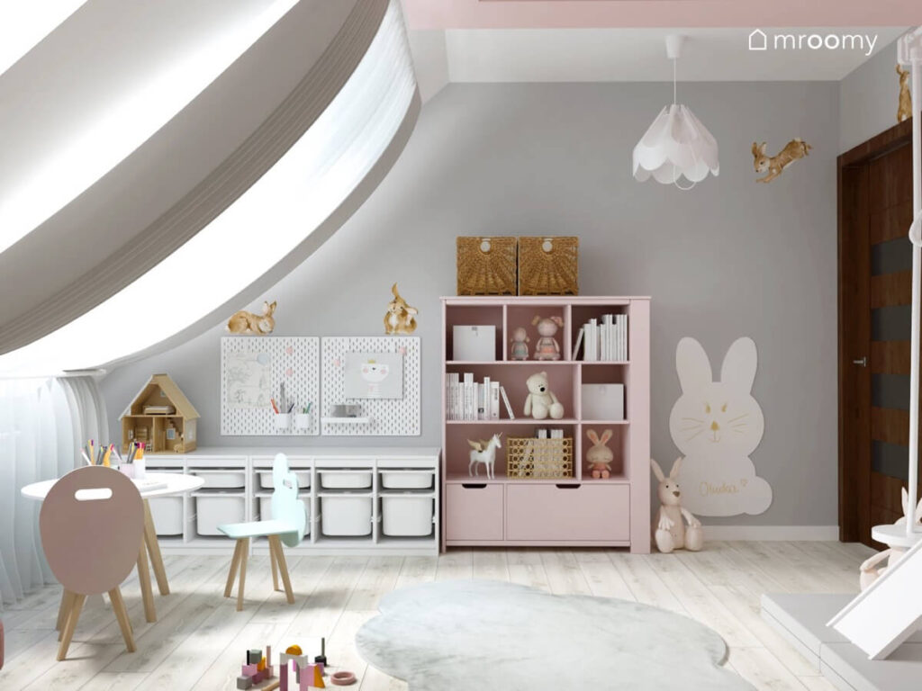 Biały regał z pojemnikami oraz różowy regał a na ścianie organizery naklejki w kształcie królików oraz tablica kredowa również w kształcie królika w pokoju dla kilkulatki