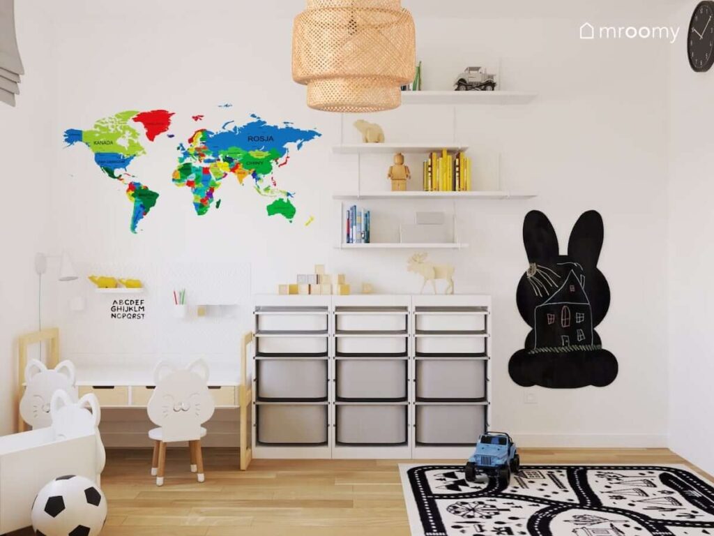 Jasny pokój dla rodzeństwa z regałem z pojemnikami na zabawki półkami ściennymi kolorową mapą świata tablicą kredową w kształcie królika oraz bambusową lampą