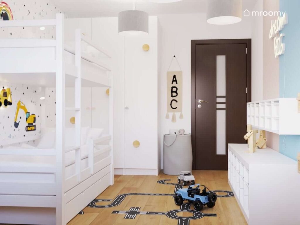 Biały pokój dla rodzeństwa z łóżkiem piętrowym oraz dużą białą szafa uzupełnioną drewnianymi wieszakami