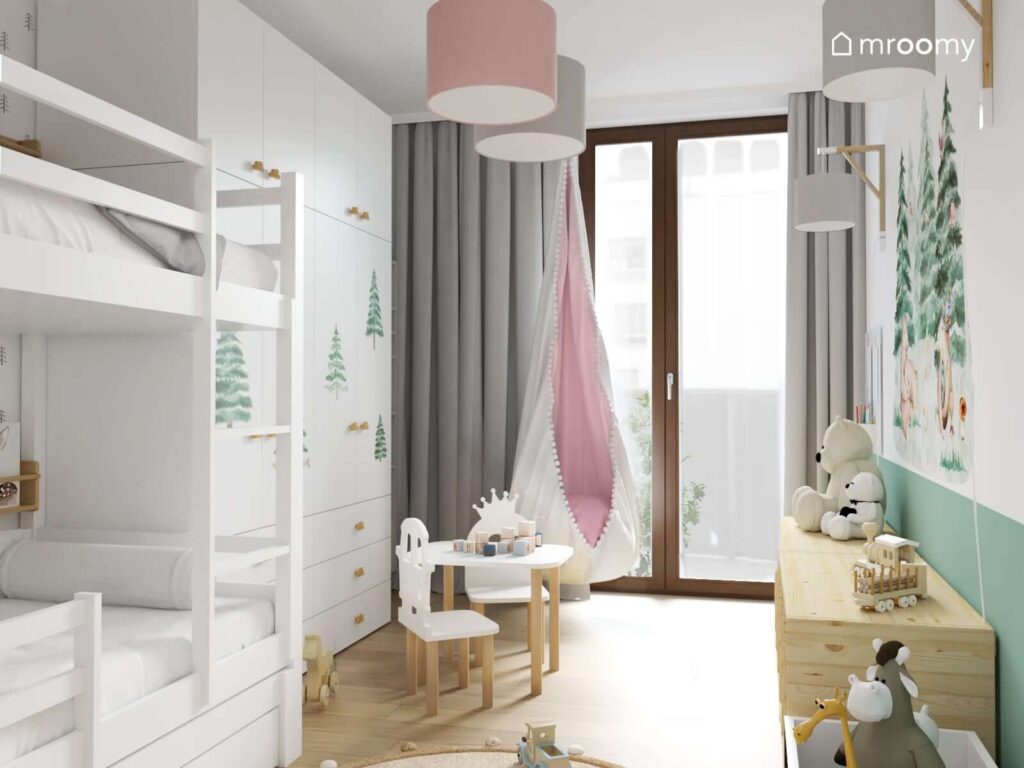 Jasny pokój dla rodzeństwa z białym łóżkiem piętrowym białą szafą uzupełnioną naklejkami w kształcie choinek oraz z szarymi zasłonami i różową huśtawką kokonem