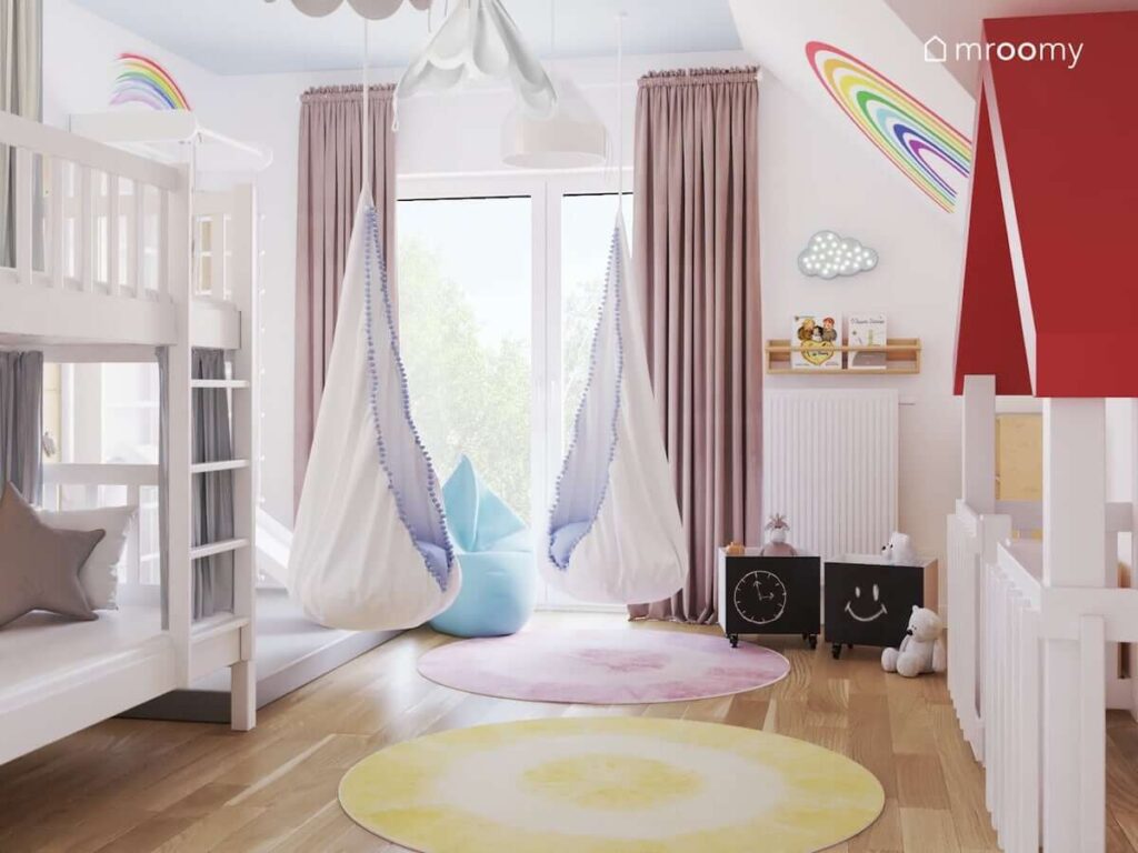 Pokój dla trzech dziewczynek a w nim dwie huśtawki kokony białe lampy bezy oraz żółty i różowy okrągły dywan