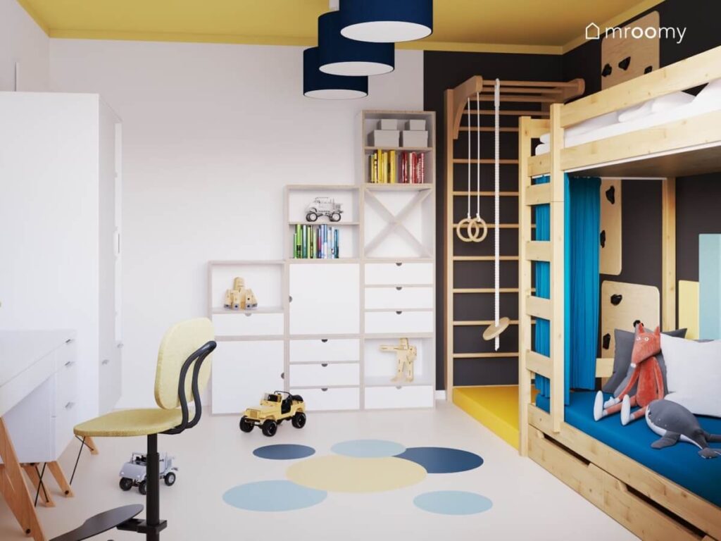 Biało czarno żółty pokój dla chłopca w wieku szkolnym z drewnianym łóżkiem piętrowym drabinką gimnastyczną biało drewnianymi szafkami oraz lampą sufitową z granatowymi abażurami