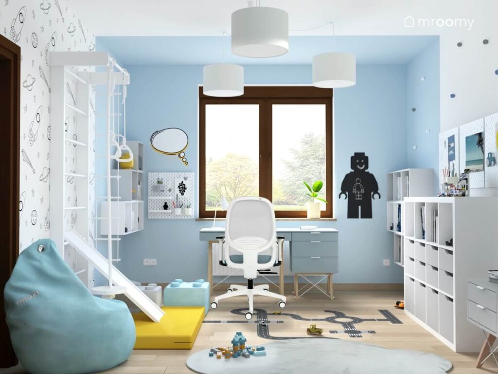 Niebieski pokój dla chłopca a w nim drabinka gimnastyczna ze zjeżdżalnią i żółtym materacem oraz niebieskie biurko z kontenerkiem na drewnianych nogach i tablica kredowa w kształcie ludzika Lego