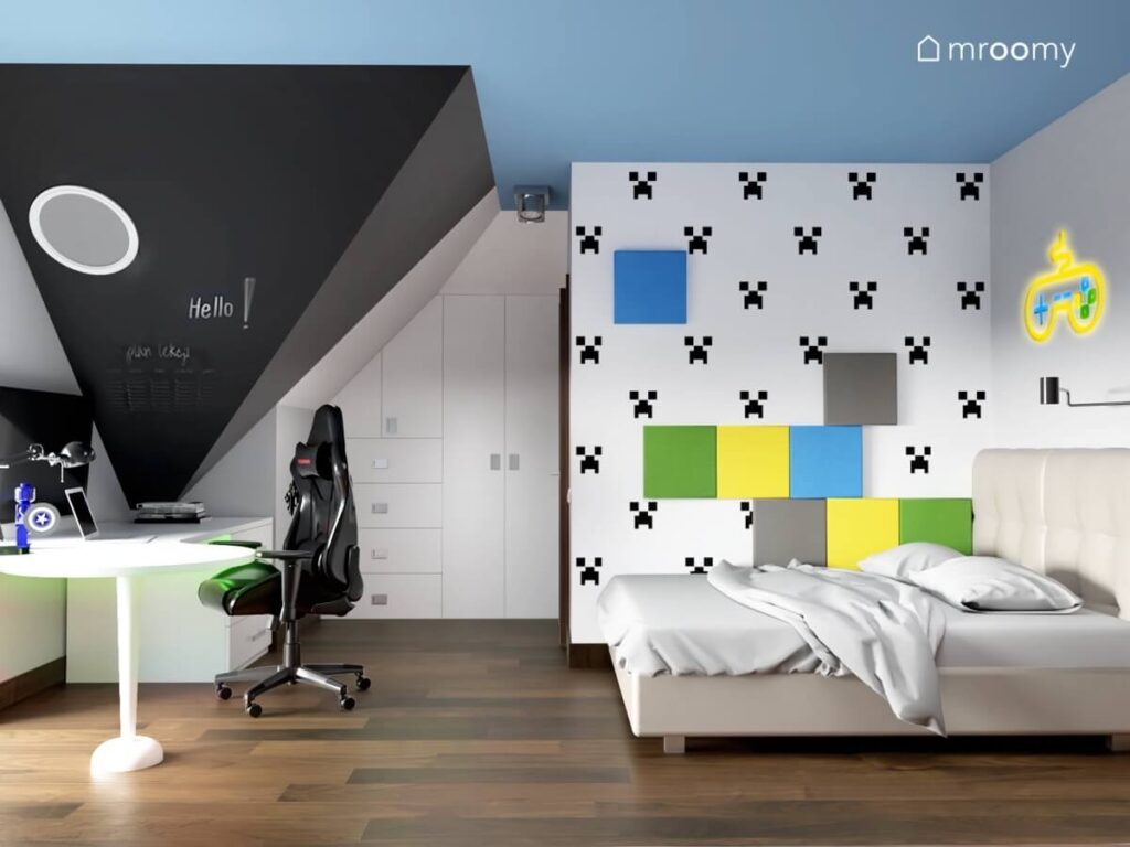 Poddaszowy pokój dla chłopca w wieku szkolnym a w nim ściana udekorowana tapetą z creeperem i panelami ściennymi w różnych kolorach a także biurko z fotelem gamingowym