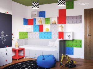 Szare łóżko a nad nim kolorowe panele w kształcie klocków oraz szafki ścienne w biało zielonym pokoju dla kilkulatka