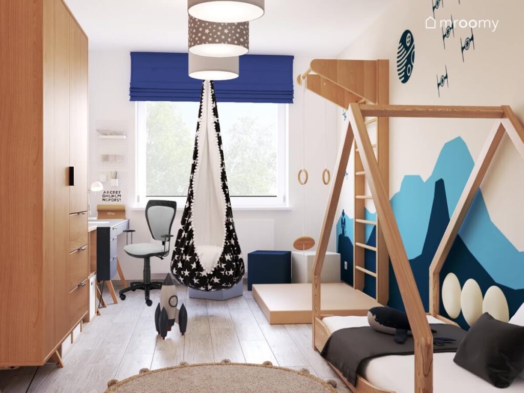 Biały pokój dla chłopca a w nim drewniana szafa łóżko domek drewniana drabinka gimnastyczna oraz biało czarna huśtawka kokon
