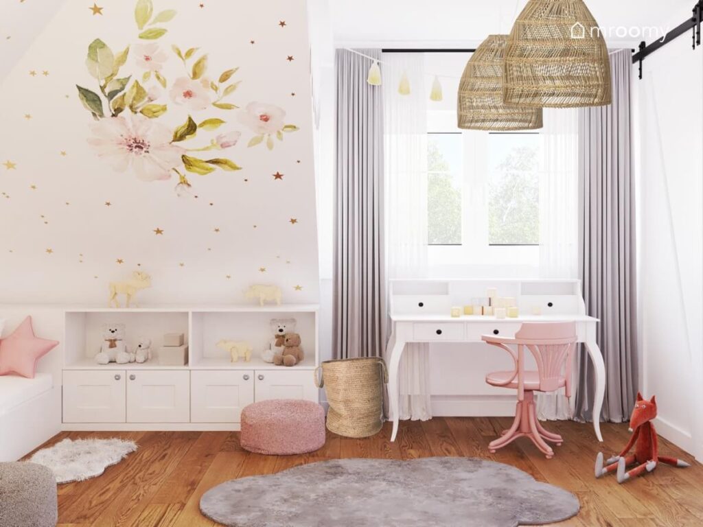 Jasny pokój dla dziewczynki z finezyjnym białym biurkiem różowym krzesłem obrotowym białymi meblami dywanikiem w kształcie chmurki koszem jutowym i rattanowymi lampami