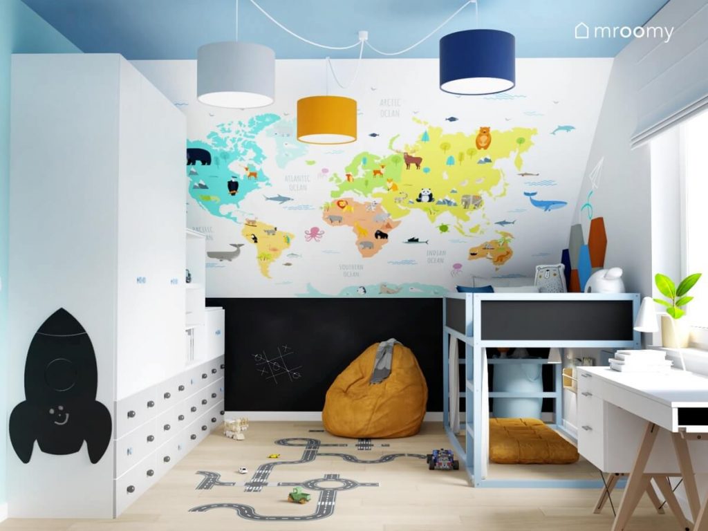 Skos ozdobiony kolorową mapą świata a także biało szara szafa modułowa łóżko z powierzchnią kredową oraz miodowy worek do siedzenia i naklejka podłogowa w kształcie jezdni w pokoju chłopca