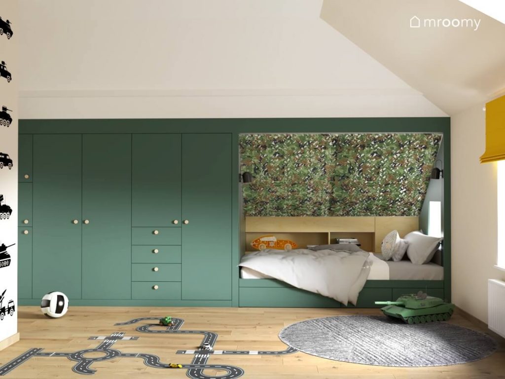 Zielona zabudowa meblowa a także łóżko z drewnianymi półkami i skosem w moro w pokoju dla chłopca w wieku szkolnym