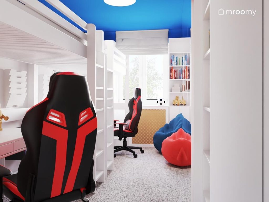 Jasny pokój dla dwóch chłopców a w nim niebieski sufit dwa łóżka na antresolach biurka z fotelami gamingowymi oraz czerwony i niebieski worek do siedzenia