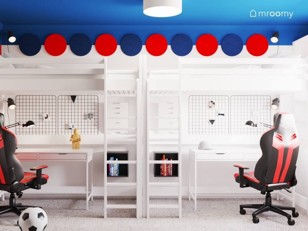 Białe łóżka na antresolach w pokoju dwóch braci a pod nimi dobrze oświetlone białe biurka z organizerami ściennymi i fotelami gaminowymi a nad nimi czerwone i niebieskie okrągłe panele ścienne