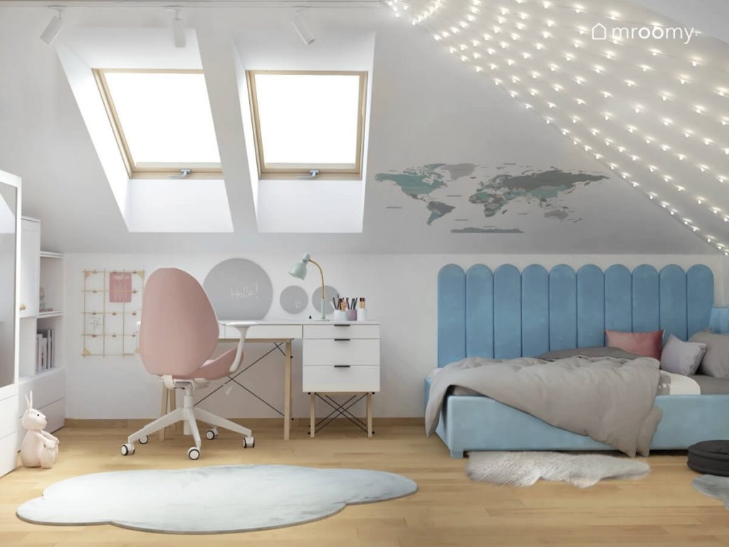 Biały poddaszowy pokój dla dziewczynki a w nim niebieskie łóżko uzupełnione panelami ściennymi w podobnym kolorze białe biurko z różowym krzesłem a na skosach mapa świata i kurtyna świetlna