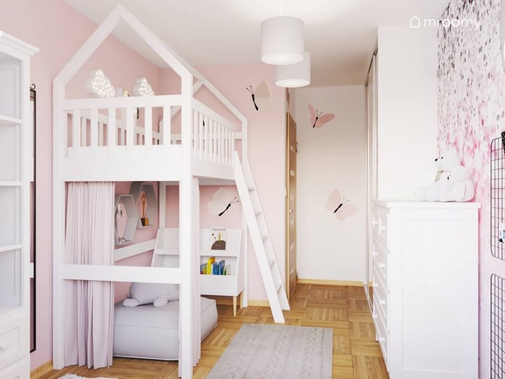 Białe łóżko domek na antresoli z przytulnym kącikiem pod spodem oraz ściany ozdobione naklejkami w kształcie motyli w biało różowym pokoju dla dziewczynki