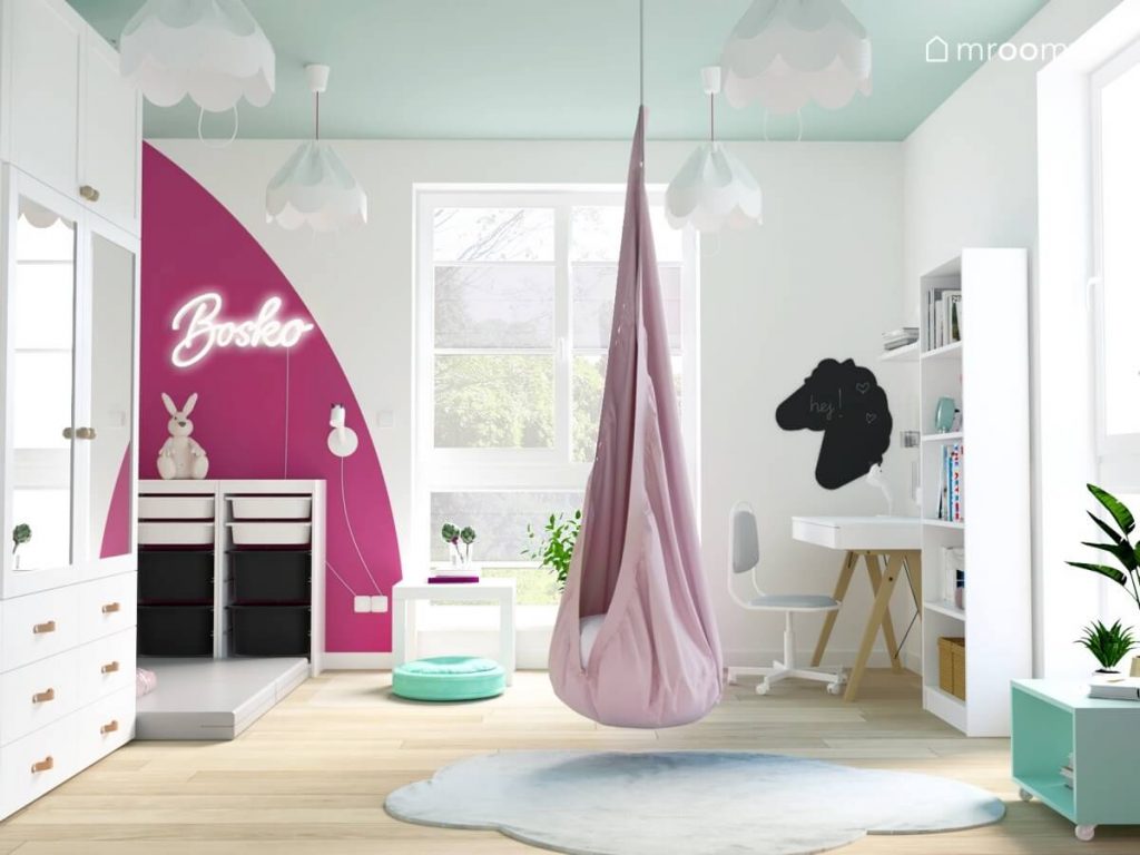 Jasny pokój dla dziewczynki z miętowym sufitem różową huśtawką kokonem regałem z pojemnikami na zabawki tablicą kredową w kształcie konia oraz dywanem w kształcie chmurki