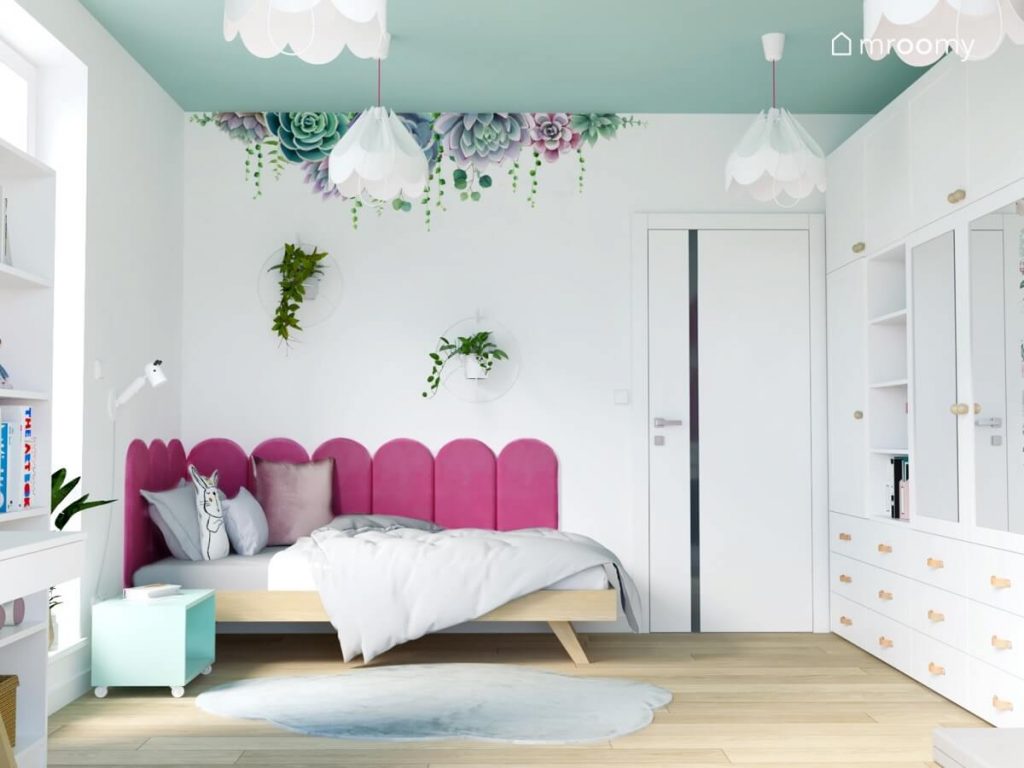 Strefa spania w pokoju dla kilkuletniej dziewczynki a w niej drewniane łóżko uzupełnione panelami ściennymi ozdobne kwietniki oraz naklejka ścienna w kształcie kwiatów