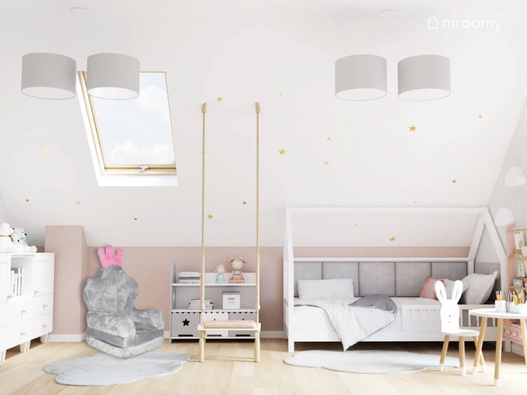 Biało różowy poddaszowy pokój dla dziewczynki z łóżkiem domkiem szarą biblioteczką huśtawką wiszącą oraz skosem ozdobionym złotymi naklejkami w kształcie gwiazdek