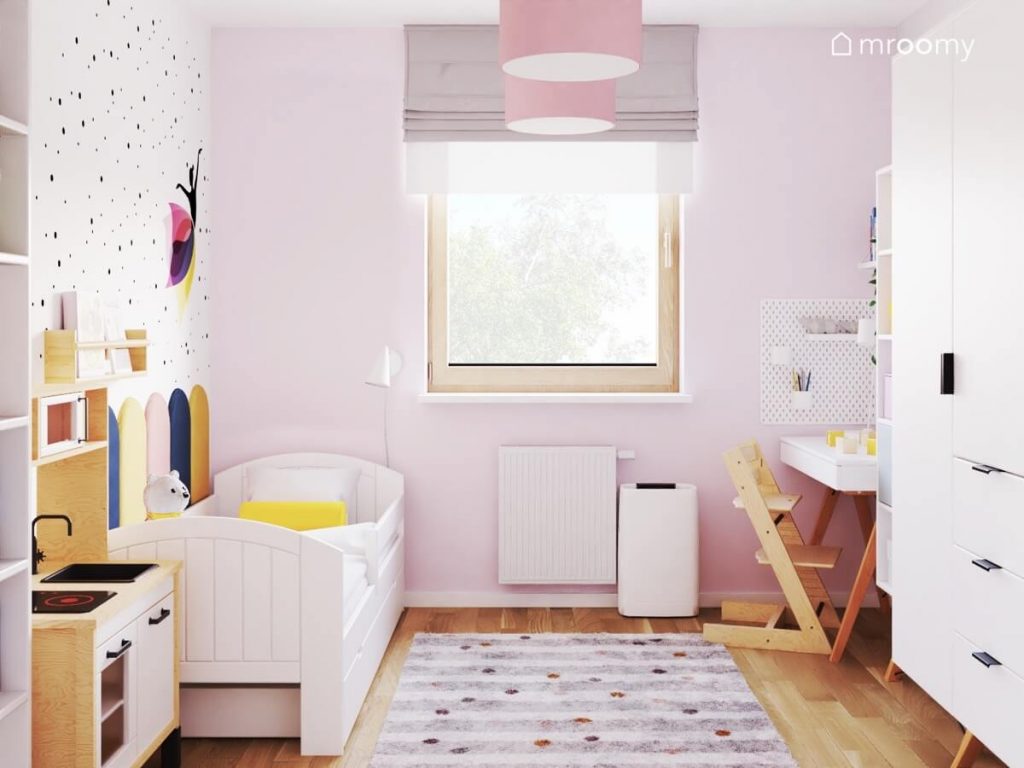 Różowo biały pokój kilkuletniej dziewczynki a w nim białe łóżko biała szafa drewniane krzesło oraz dywan w paski i kropki