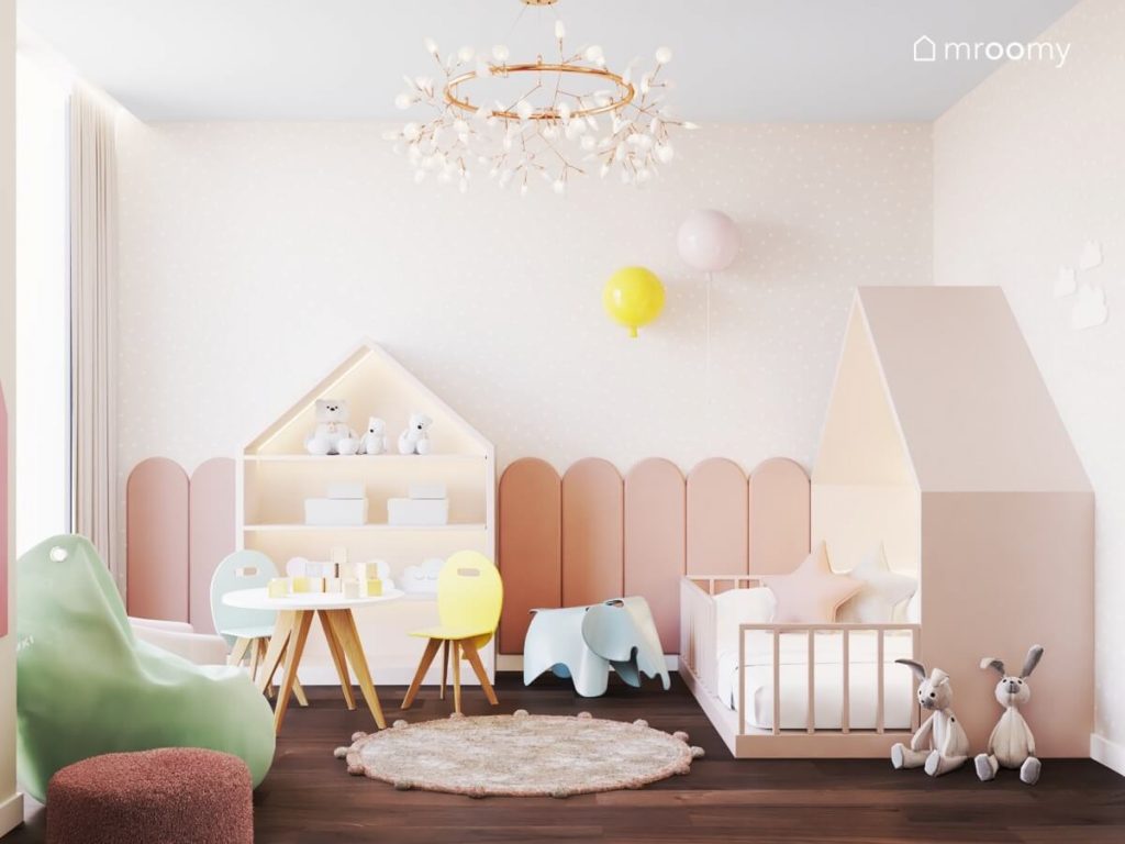 Regał i łóżko w kształcie domku a także krzesełka z oparciami w kształcie balonów i kinkiety balony w jasnym pokoju dla dziewczynki pokrytym tapetą w kropki