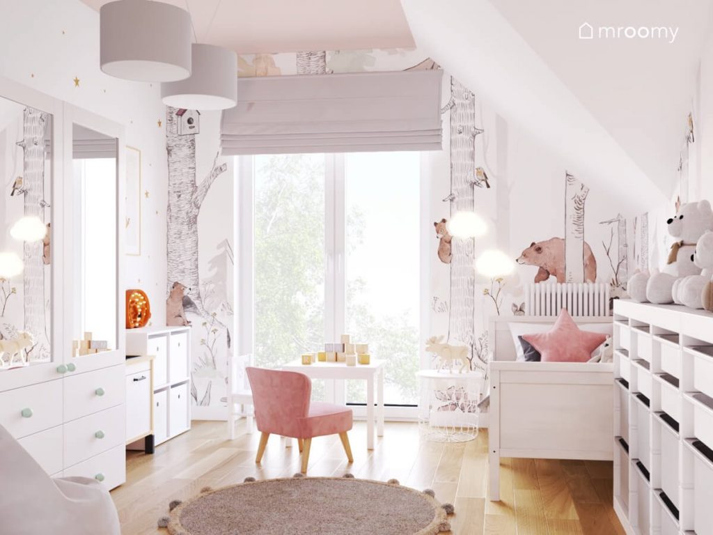 Jasny pokój dla małej dziewczynki a w nim białe meble stolik z różowym fotelikiem a na ścianie tapeta z leśnym motywem i lampki w kształcie chmurek