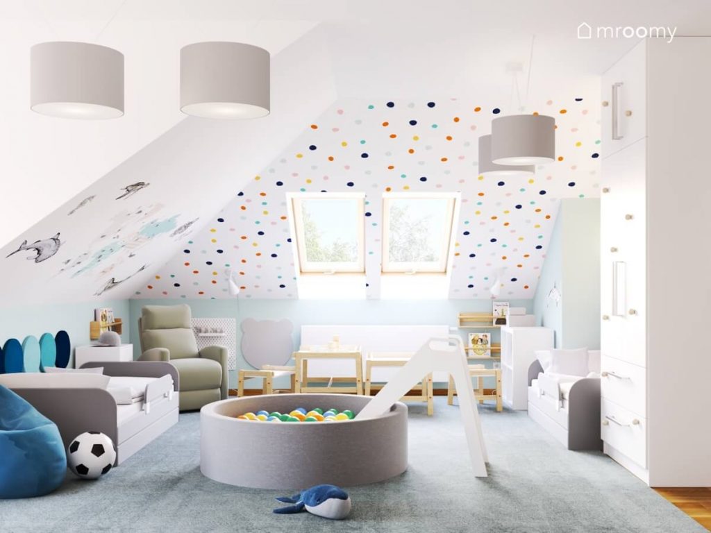 Biały poddaszowy pokój dla rodzeństwa a w nim skosy ozdobione kolorowymi kropkami oraz mapą świata a także dwa szare łóżka basen z kulkami i dwa małe stoliki z krzesełkami