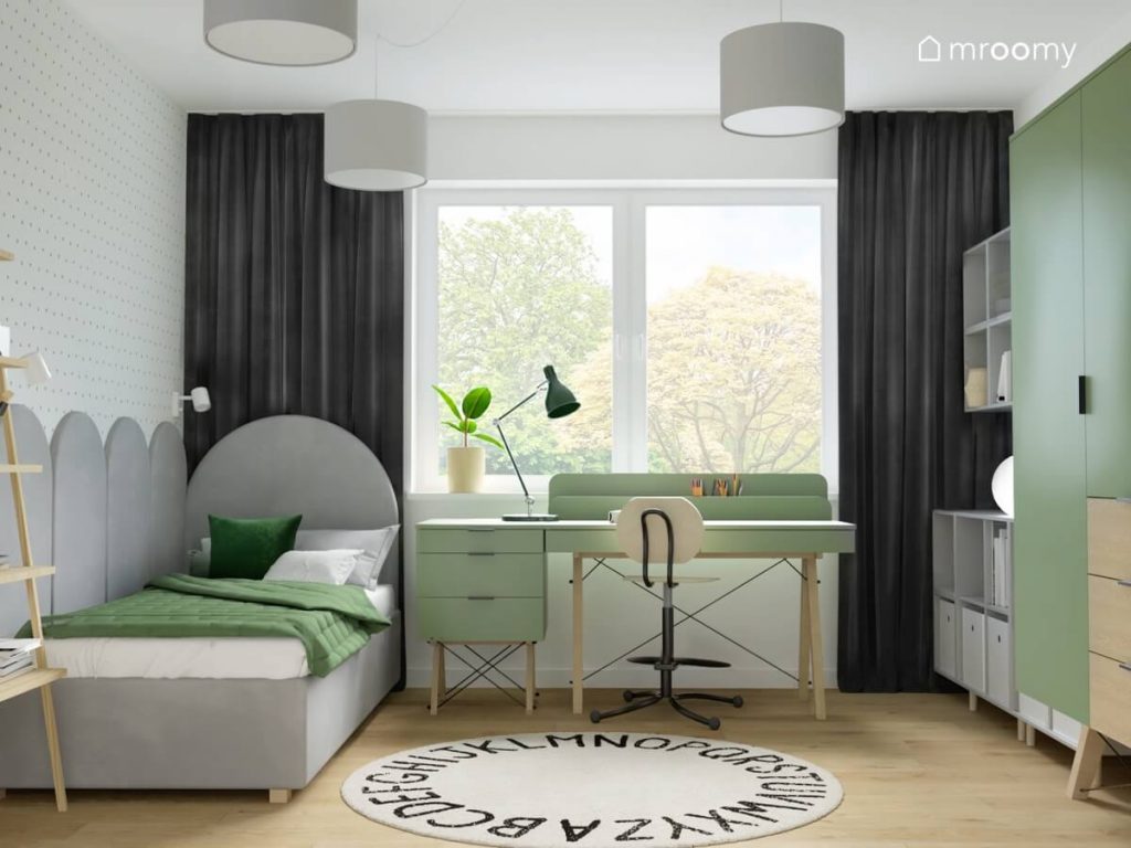 Szare tapicerowane łóżko zielone biurko z kontenerkiem a także dywan dywan z alfabetem i szare zasłony w pokoju dla chłopca