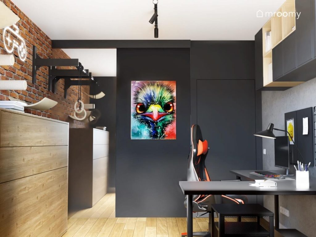 Młodzieżowy pokój dla chłopca a w nim czarna szafa z lustrzanym frontem i ozdobnym plakatem ze strusiem drewniana komoda i biurko z fotelem gamingowym