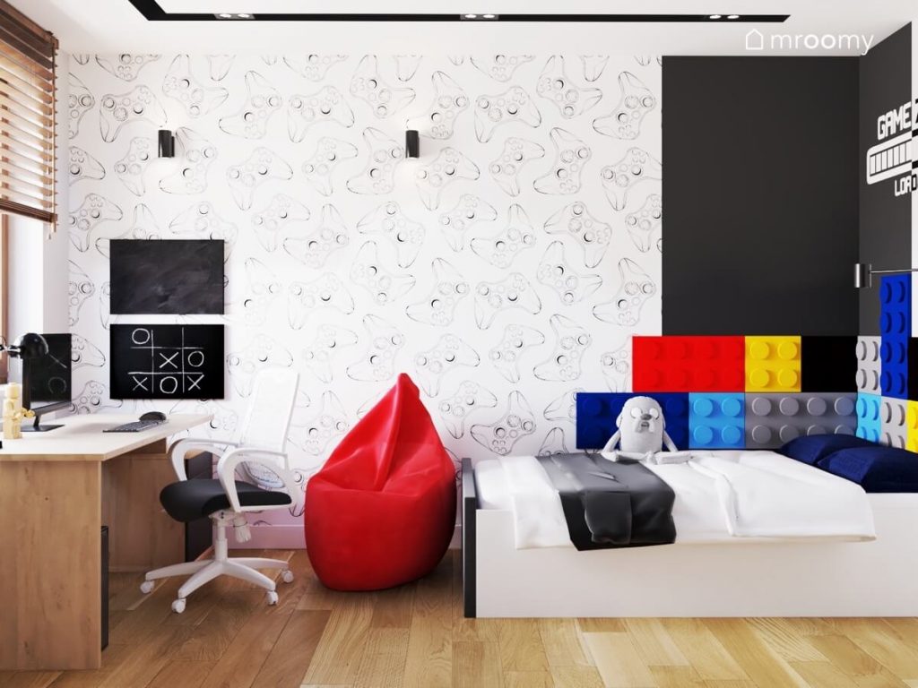 Strefa nauki z tablicami kredowymi oraz strefa spania z łóżkiem uzupełnionym kolorowymi panelami w kształcie klocków a na ścianie gamingowa tapeta w pokoju dla chłopca