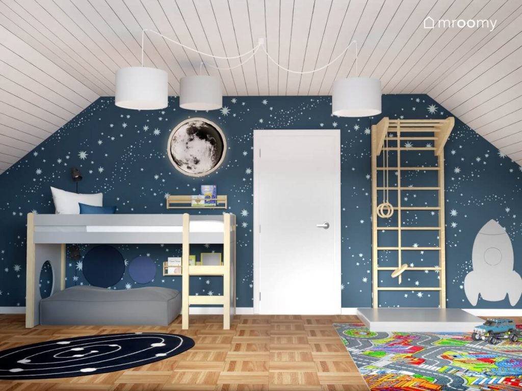 Łóżko na antresoli z miejscem do odpoczynku pod spodem a także ściana pokryta kosmiczną tapetą a na niej drewniana drabinka gimnastyczna oraz lampa w kształcie księżyca w pokoju dla chłopca