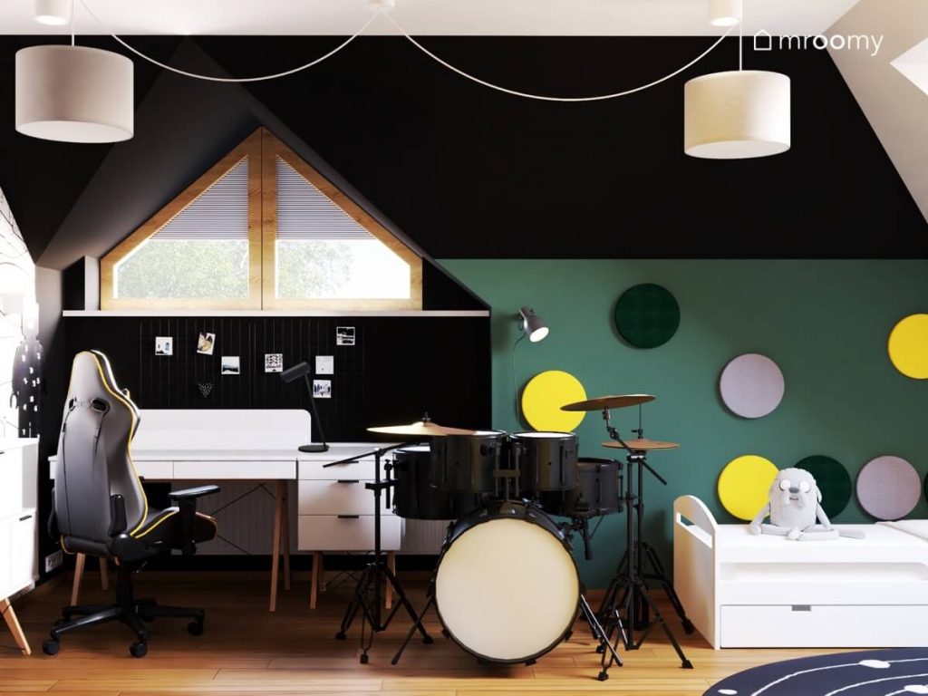 Czarno zielony poddaszowy pokój dla chłopca w wieku szkolnym a w nim białe meble perkusja oraz kolorowe panele ścienne.