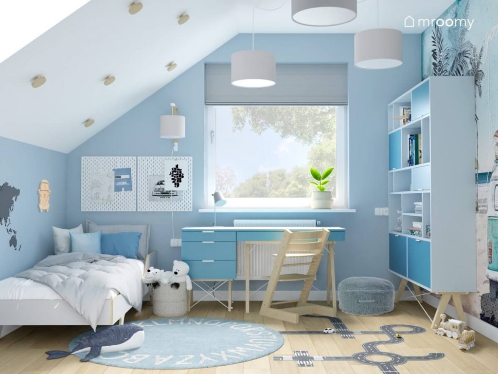 Biało niebieski poddaszowy pokój dla małego chłopca a w nim białe i niebieskie meble z drewnianymi elementami oraz dywan z alfabetem i naklejka podłogowa w kształcie jezdni