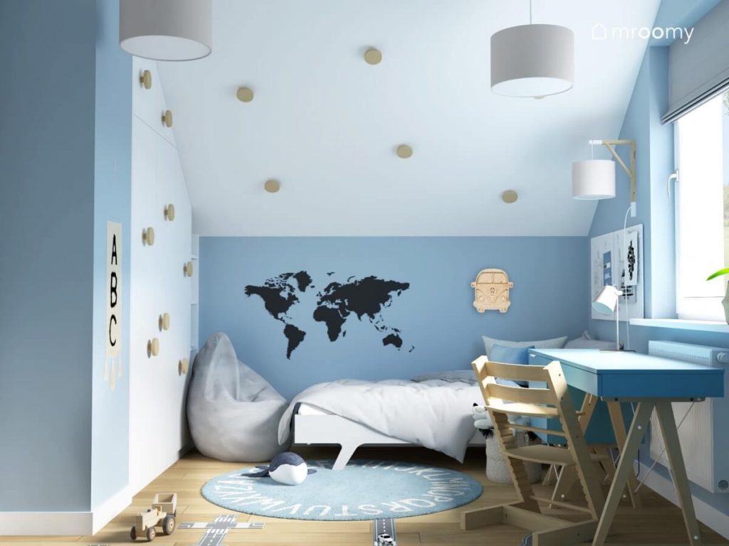 Niebiesko biały poddaszowy pokój dla chłopca a w nim biała szafa niebieskie biurko z drewnianym krzesłem szara pufa i łóżko nad którym wisi drewniana lampka w kształcie samochodu i naklejka w kształcie mapy świata