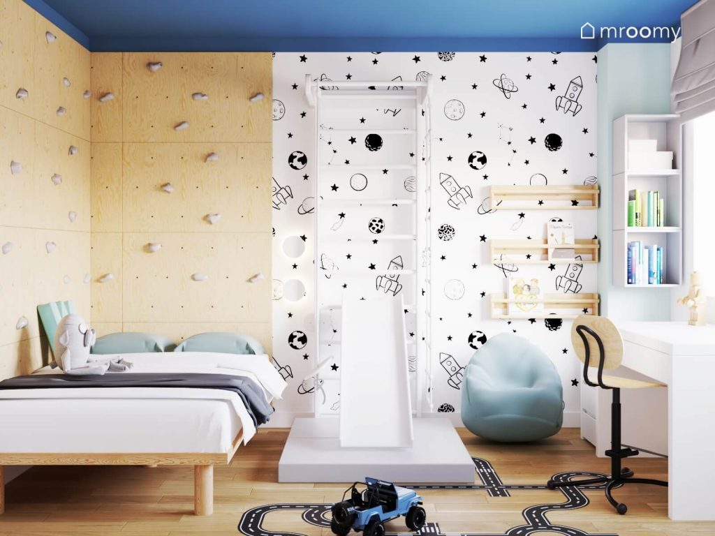 Drewniane łóżko ścianka wspinaczkowa ze sklejki oraz biała drabinka gimnastyczna ze zjeżdżalnią a na ścianie kosmiczna tapeta w pokoju dla chłopca