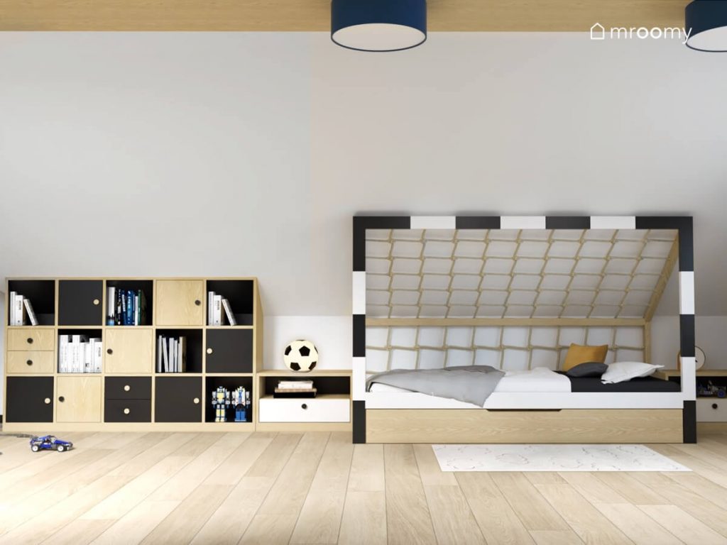 Strefa spania w poddaszowym pokoju dla ośmiolatka a w niej łóżko w kształcie bramki do piłki nożnej oraz czarno drewniana szafka