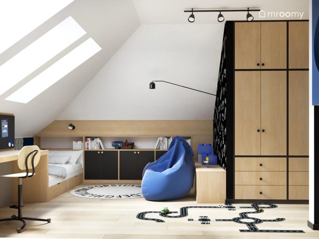 Jasny poddaszowy pokój dla chłopca z czarno drewnianymi meblami niebieskimi pufami samo oraz dywanem z alfabetem i naklejką podłogową w kształcie ulicy