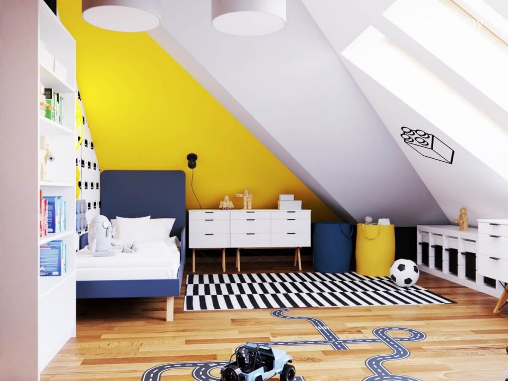 Kolorowy poddaszowy pokój dla chłopca a w nim granatowe łóżko biała komoda na drewnianych nogach worki na zabawki oraz czarno biały dywan i naklejka podłogowa w kształcie jezdni