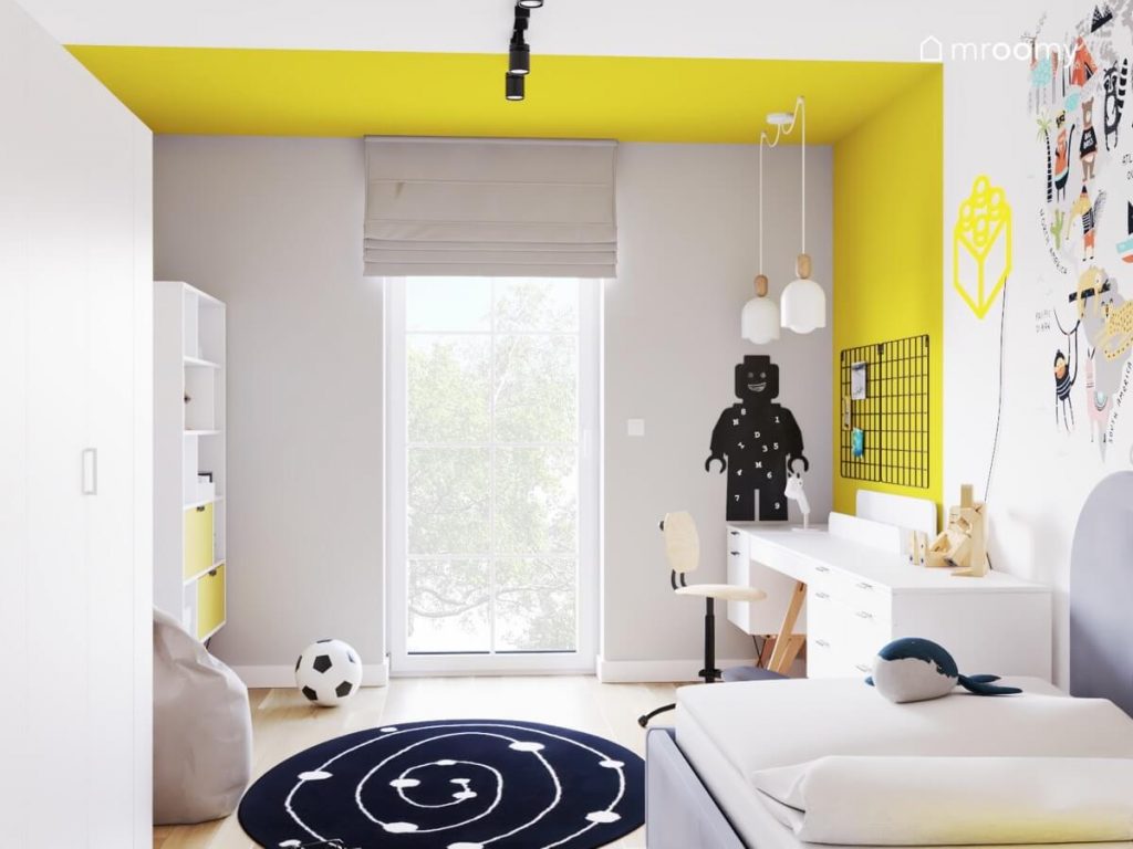 Biało szaro żółty pokój chłopca a w nim białe meble tablica kredowa w kształcie ludzika Lego i galaktyczny dywan