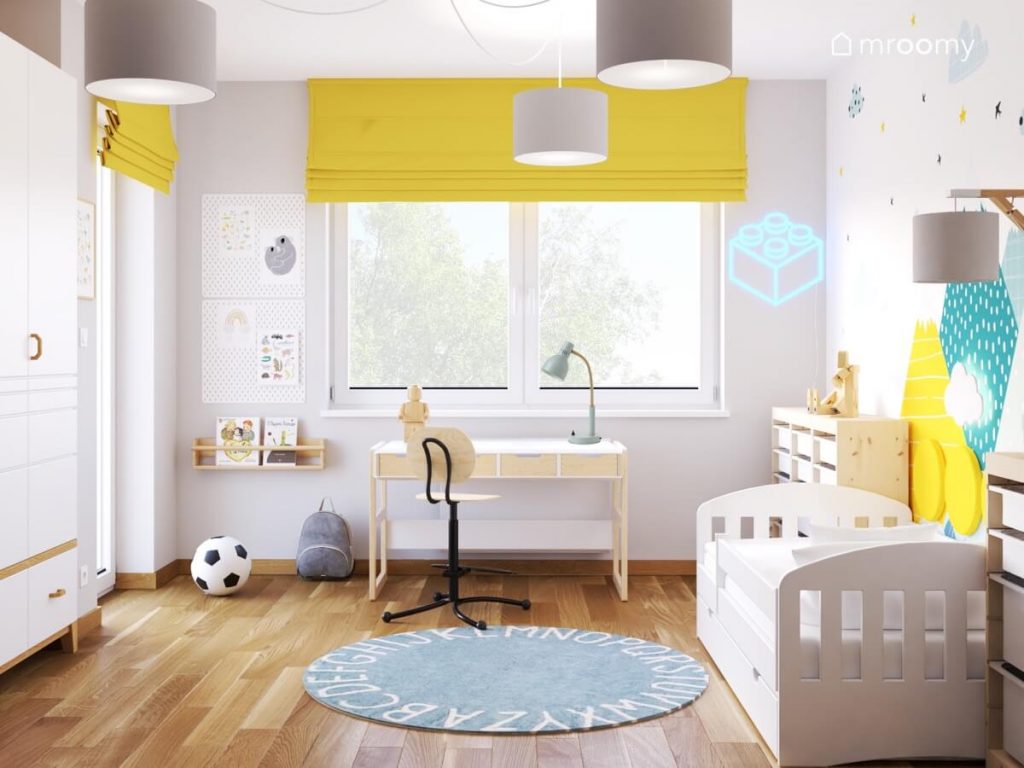 Biało szary pokój małego chłopca a w nim białe i drewniane meble niebieski dywan z alfabetem żółte rolety oraz ledon w kształcie klocka