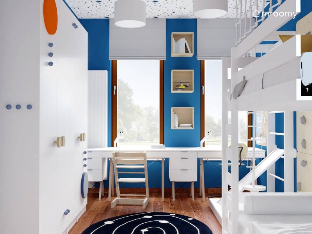 Biało niebieski pokój dwóch chłopców a w nim białe biurka na drewnianych nogach z kontenerkiem i drewnianymi krzesłami a na ścianie drewniane szafki ścienne