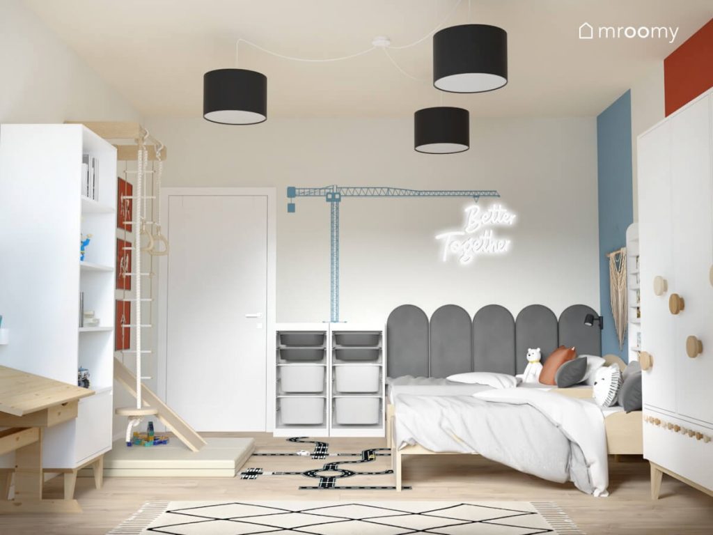 Białe i drewniane meble w pokoju dwóch chłopców a na ścianie ledon jakby zawieszony na naklejce w kształcie dźwigu a na suficie lampa z trzema czarnymi abażurami