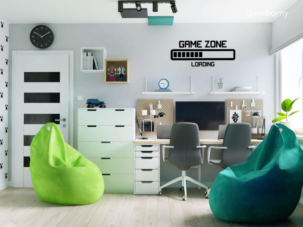 Strefa nauki w biało szarym pokoju dwóch chłopców a tam długie biurko z organizerami i półkami ściennymi oraz dwie pufy w różnych odcieniach zieleni