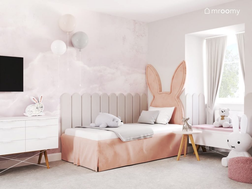 Różowe łóżko z zagłówkiem w kształcie królika uzupełnione szarymi panelami ściennymi a nad nim kinkiety w kształcie balonów w pokoju kilkuletniej dziewczynki