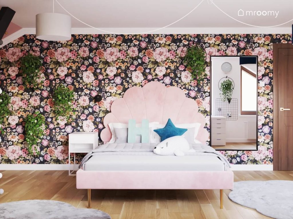 Różowe łóżko z ozdobnym zagłówkiem a za nim kwiecista tapeta ozdobne kwietniki oraz lustro w pokoju dla dziewczynki w wieku szkolnym