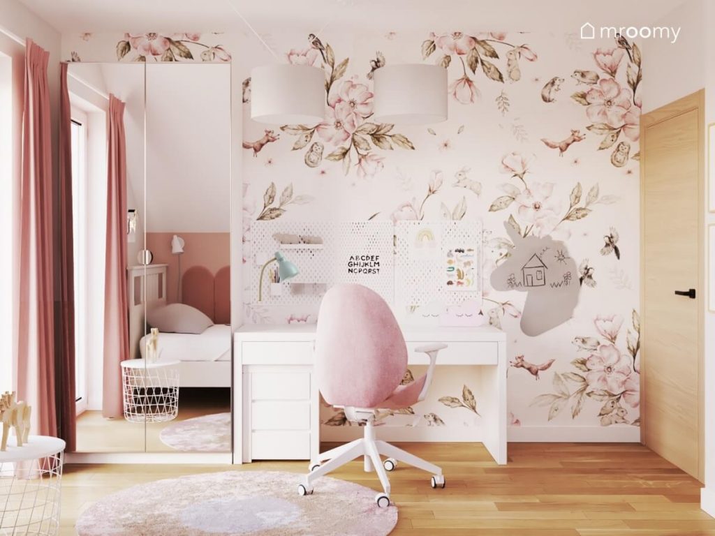 Strefa nauki w pokoju dla dziewczynki ze ścianą oklejoną tapetą w kwiaty a w niej białe biurko z organizerami tablica kredowa w kształcie jednorożca oraz szafa z lustrzanymi frontami