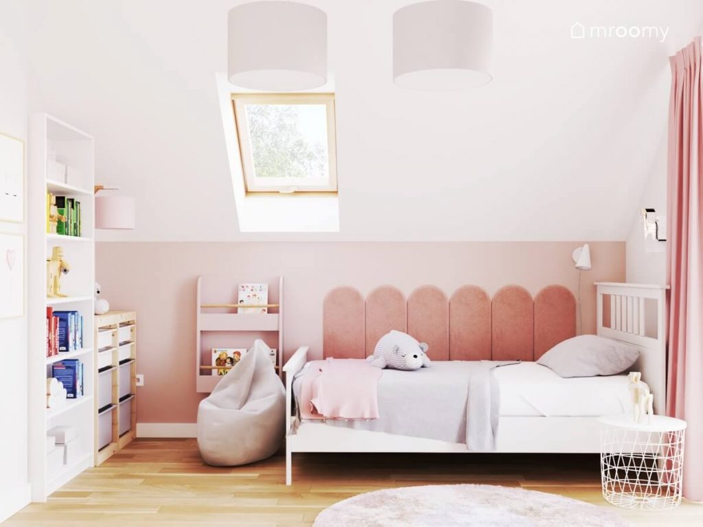 Strefa spania w biało różowym poddaszowym pokoju dla dziewczynki z białym łóżkiem uzupełnionym panelami ściennymi oraz różową biblioteczką