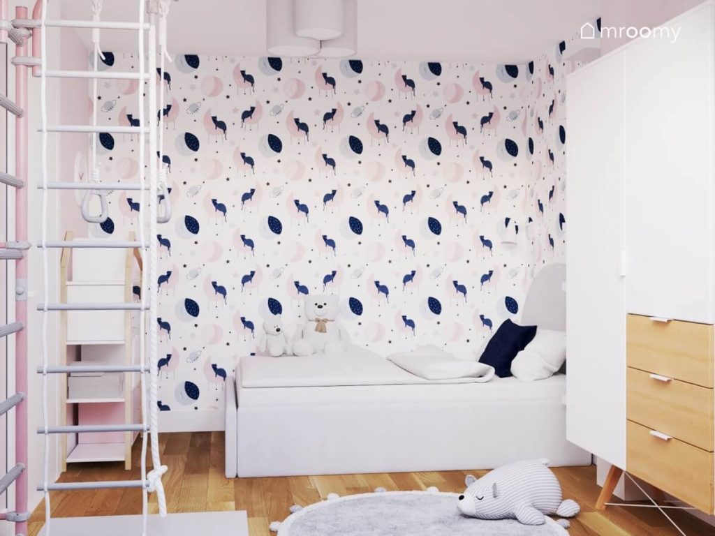 Strefa spania w pokoju dla dziewczynki z szarym łóżkiem i ścianą pokrytą urokliwą tapetą w księżyce