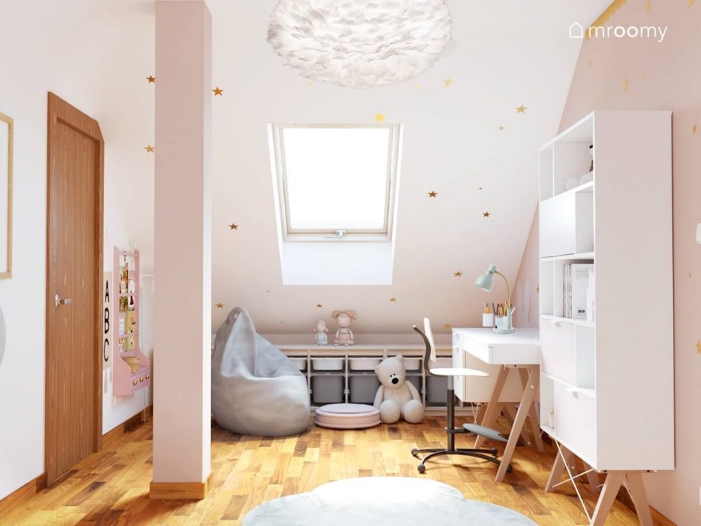 Biało różowy poddaszowy pokój dla dziewczynki a w nim białe meble podłużny regał z pojemnikami na zabawki oraz skos ozdobiony złotymi gwiazdkami
